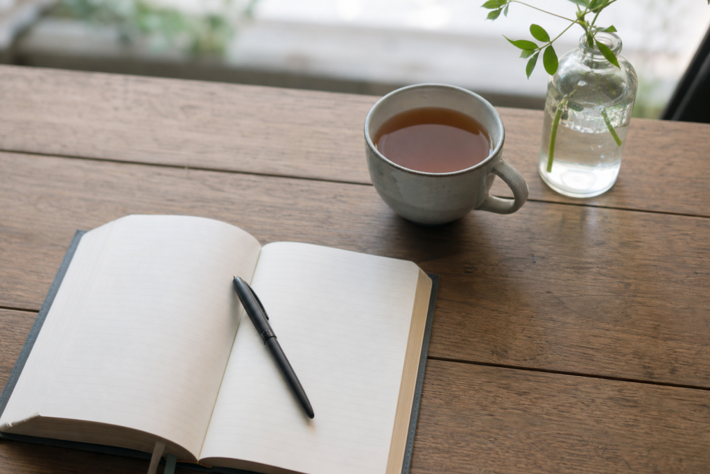Open notebook with pen and cup of tea on a simple wooden table