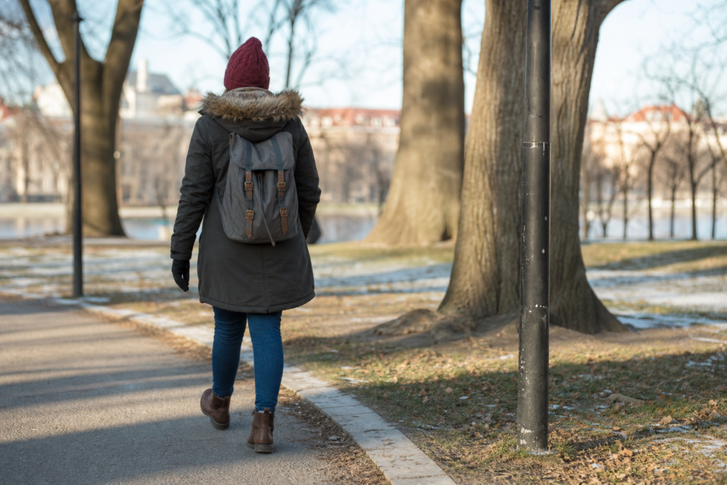 person bundled in winter clothes walking through a bright park during daytime