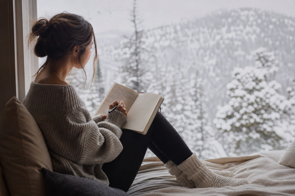 Person reflecting in a journal by a window during winter