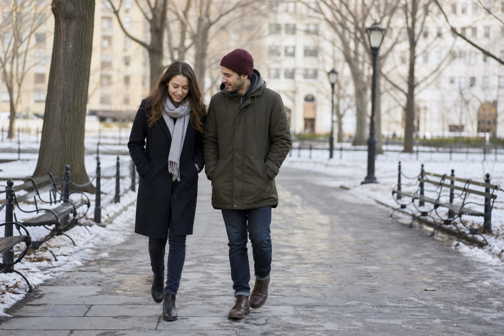 Two adults in coats walking together in a park during winter daylight